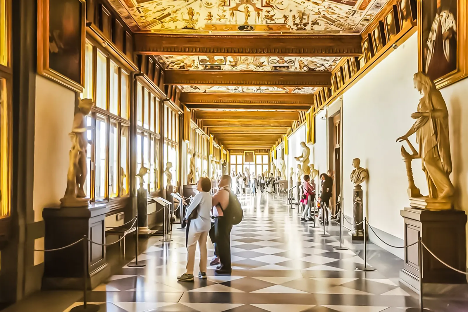 Visitors strolling the Uffizi corridor beneath its frescoed ceiling