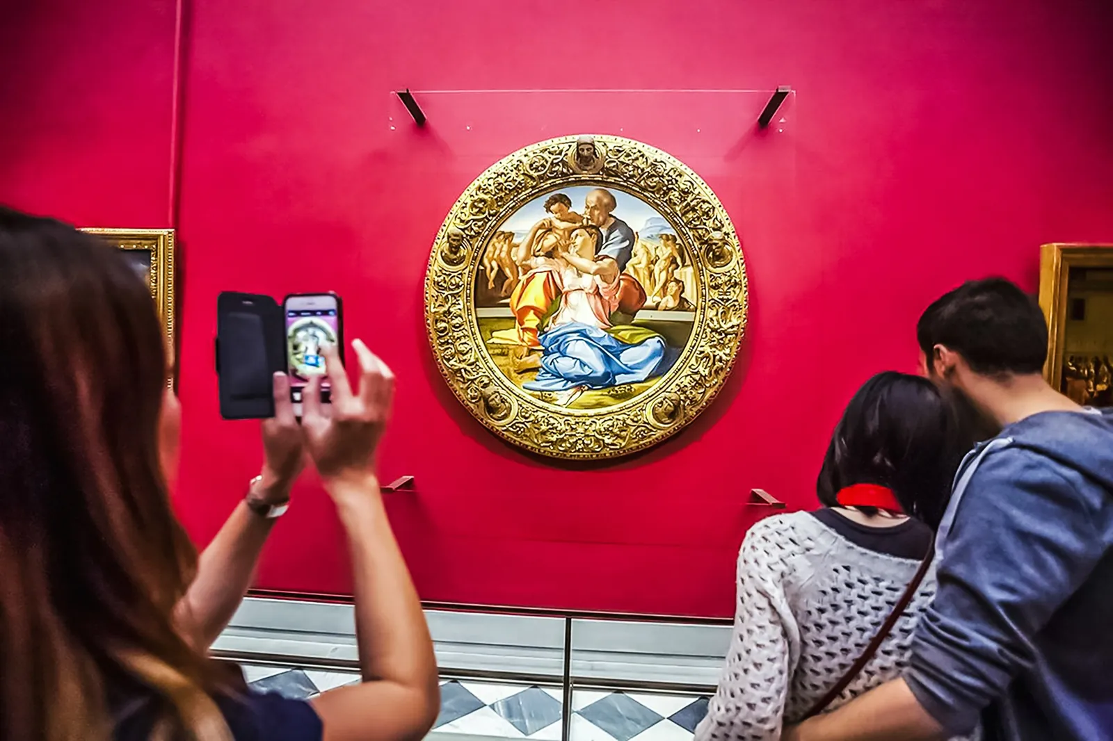 Visitors photographing Michelangelo's Doni Tondo on its red wall