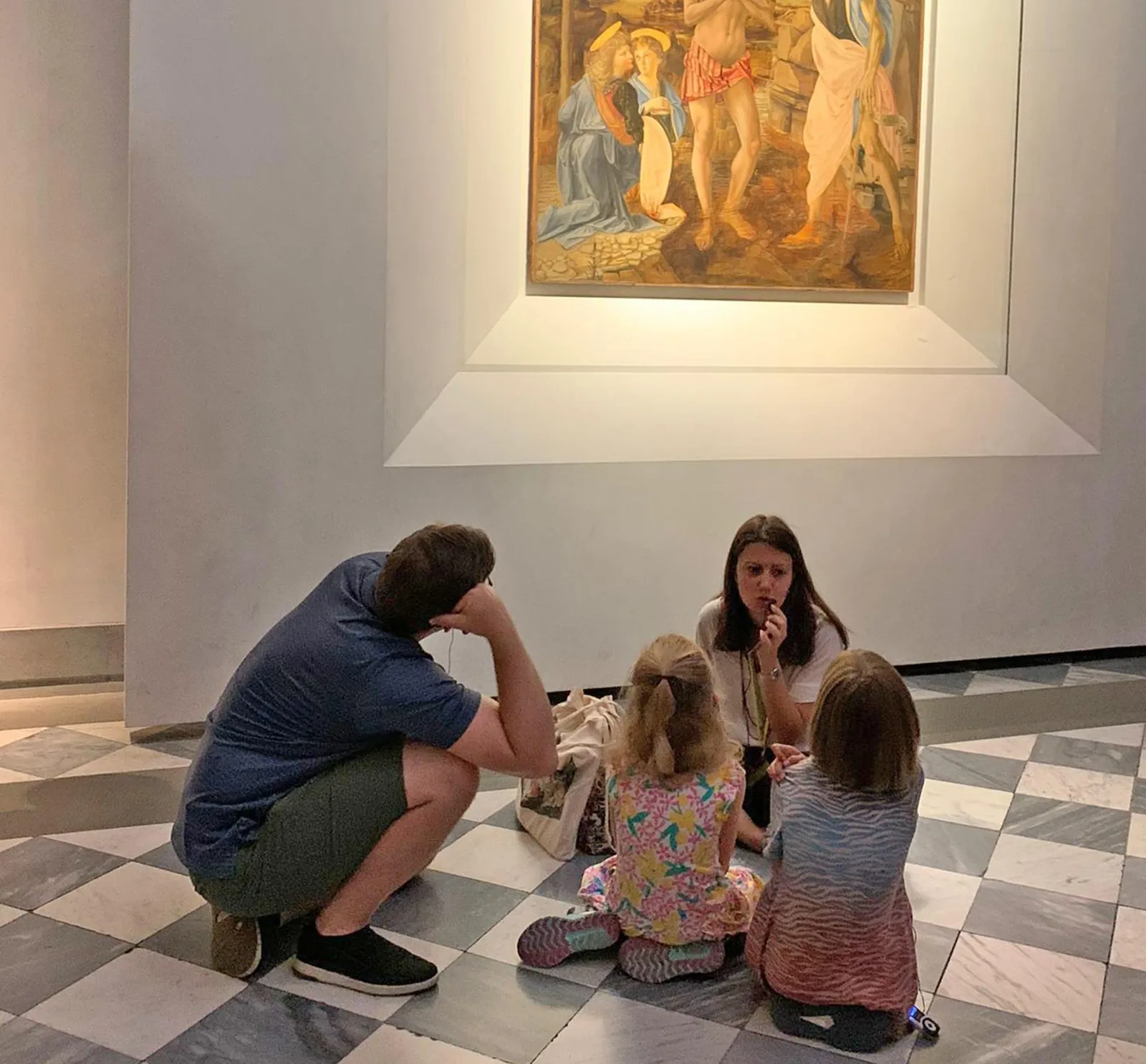 Guide sitting on the gallery floor with children in front of a Botticelli painting