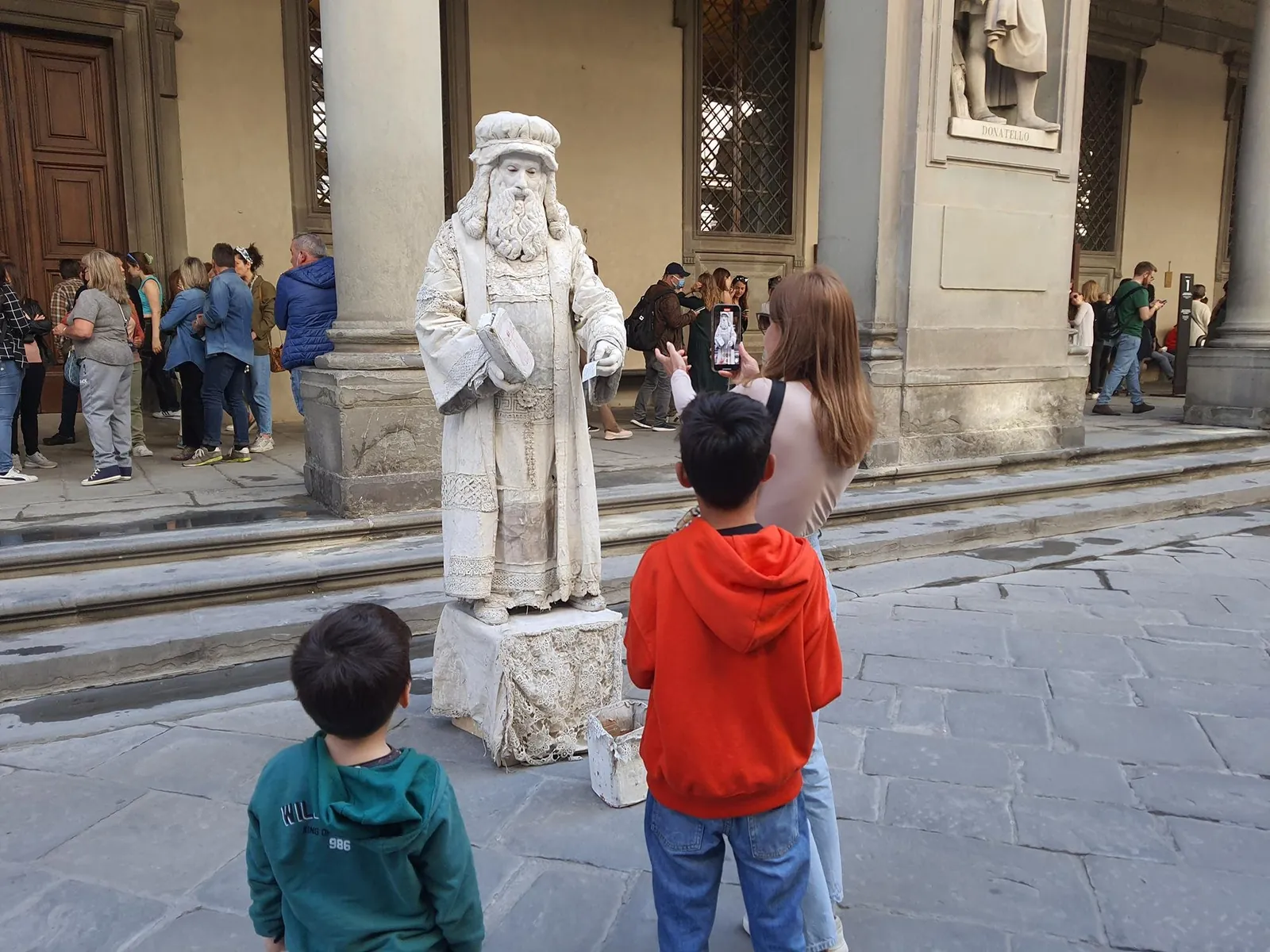Children looking up at the statue of Leonardo da Vinci in the Uffizi loggia